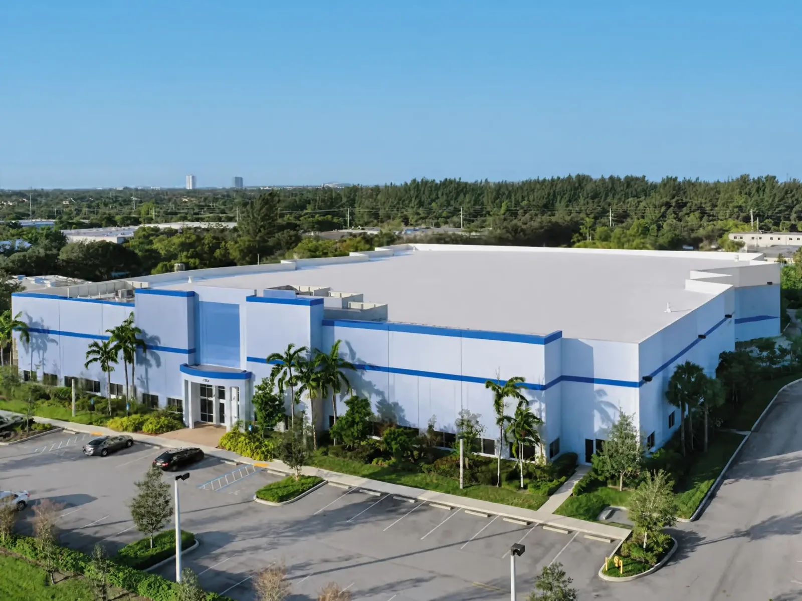 Aerial view of a large white single-tenant industrial building with palm trees and a truck court